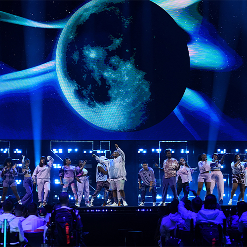 Performers on stage at the national lottery homecoming event at AO arena with interstellar visuals behind on a display screen.